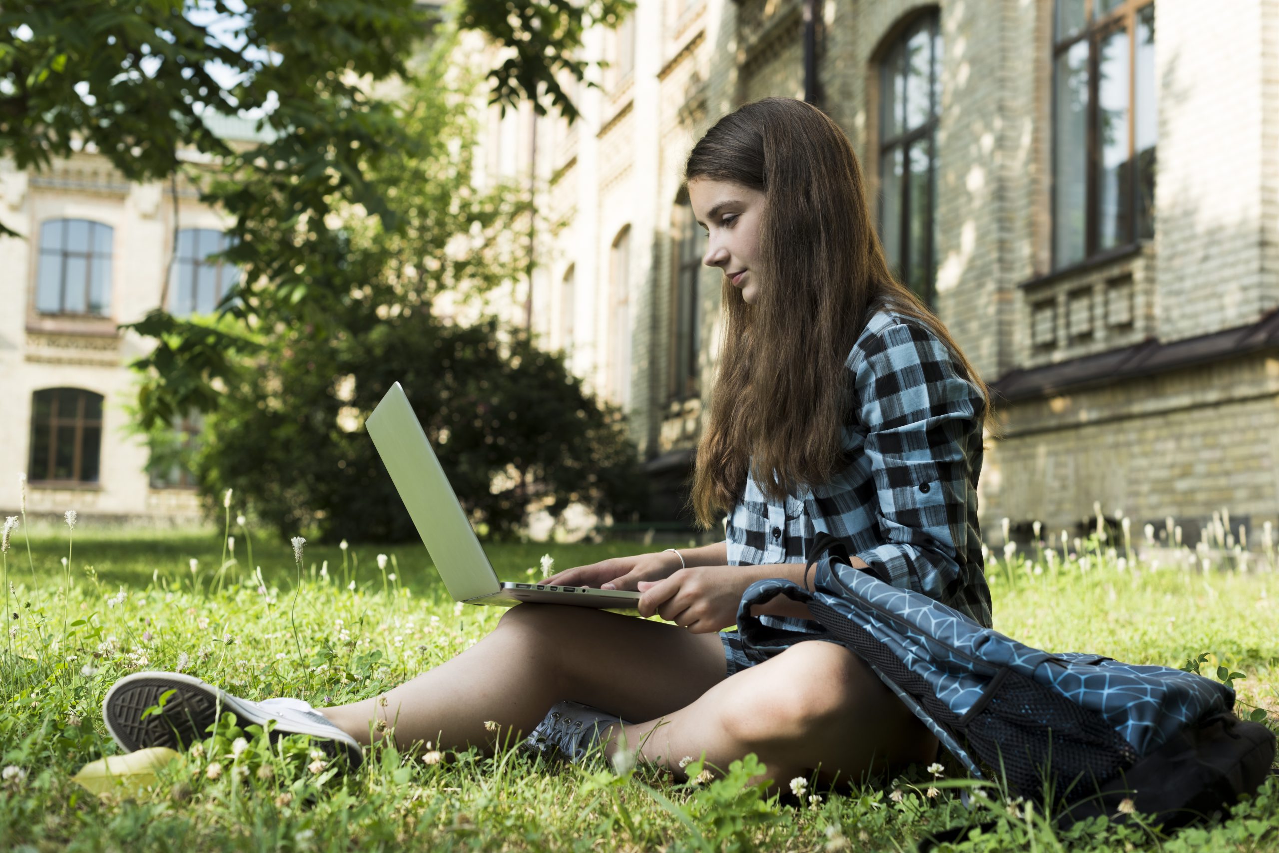 jovem estuda sentada na grama com notebook no colo